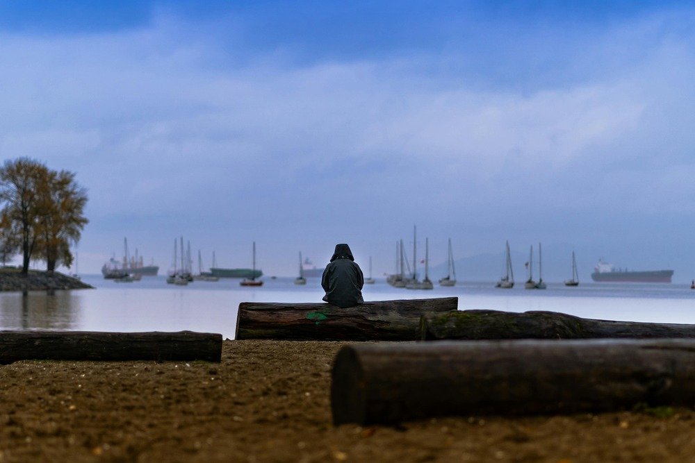 Pessoa sentada em um tronca a beira do mar